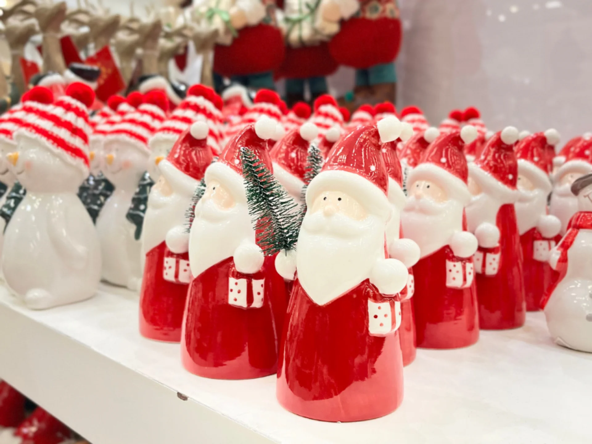 vários Papai Noel de cerâmica com um galho de planta na mão e uma cestinha na outra.
